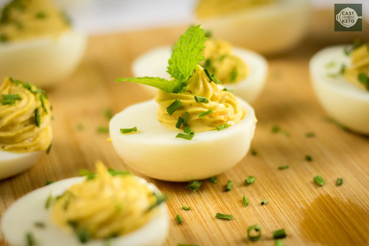 Close up of keto deviled eggs topped with chives and mint leaves.