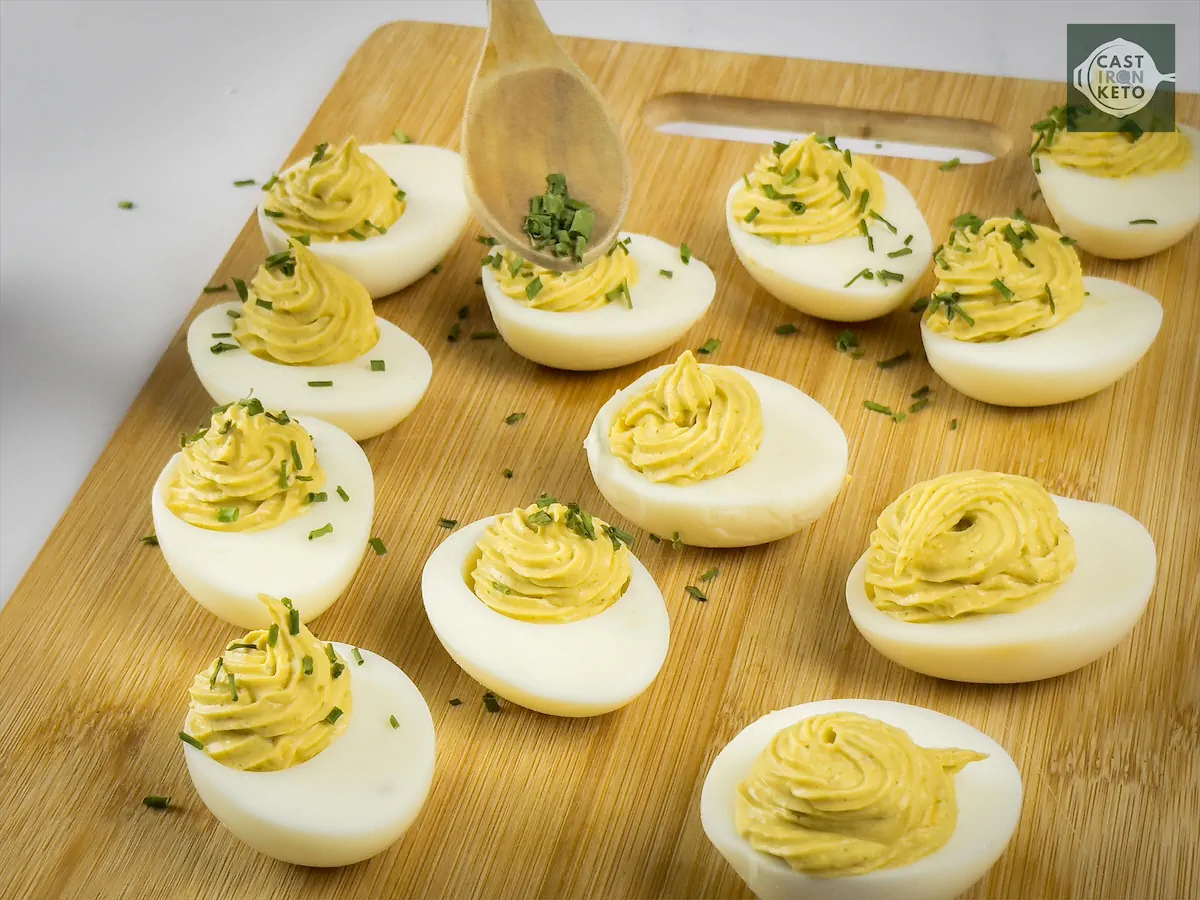 Topping the keto deviled eggs with finely cut chives using a spoon.