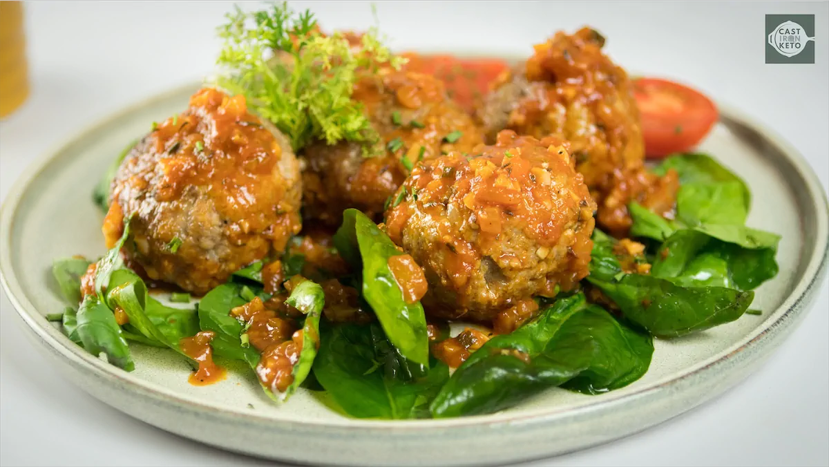 Italian meatballs recipe on a plate featuring greens and tomatoes.
