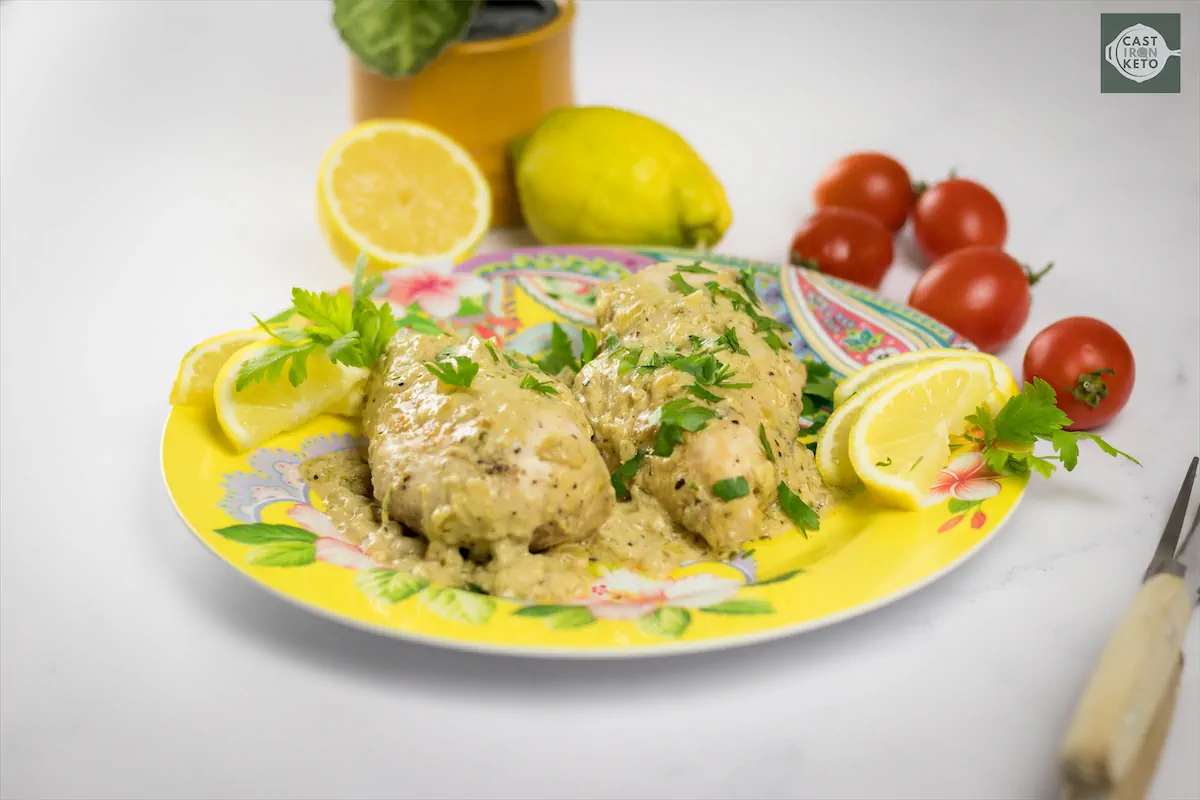 Lemon pepper chicken recipe served on a plate on a kitchen table with other vegetables like tomatoes and lemons.