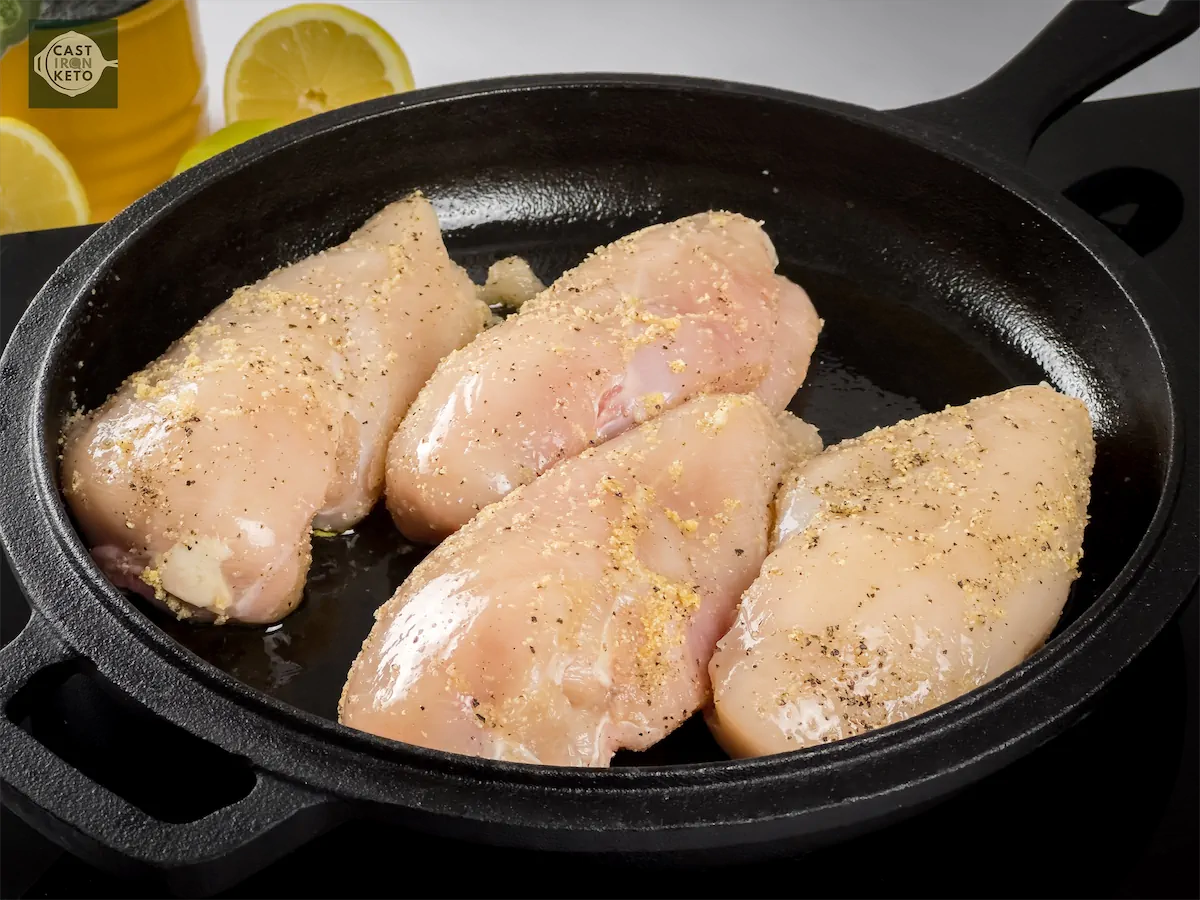 Seasoned chicken breasts being cooked in cast iron pan.