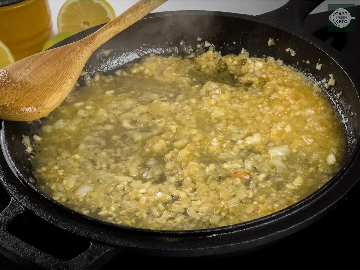 Onions, garlic, and lemon juice being cooked in melted butter in a cast iron pan.