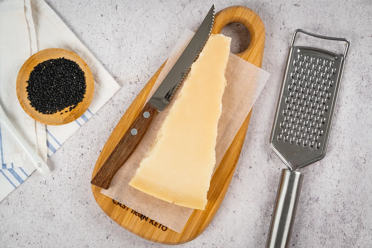 Slice of parmesan cheese, black seeds, and grater made ready on kitchen table.
