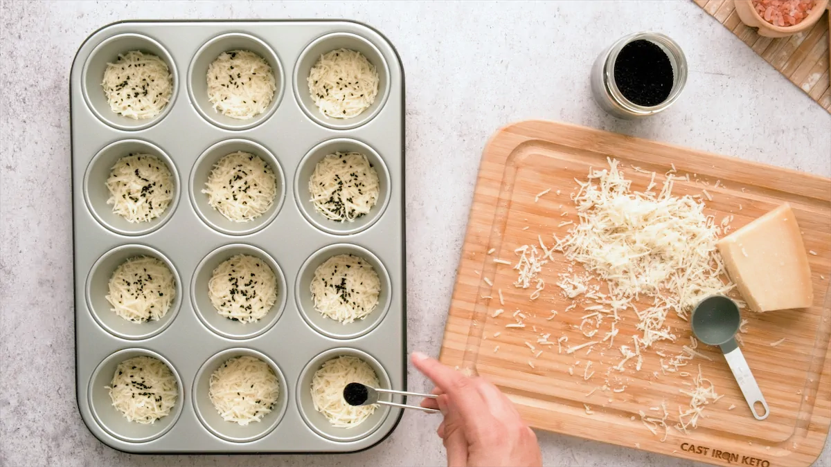Adding black seeds over grated cheese on each vessels of the muffin tin.