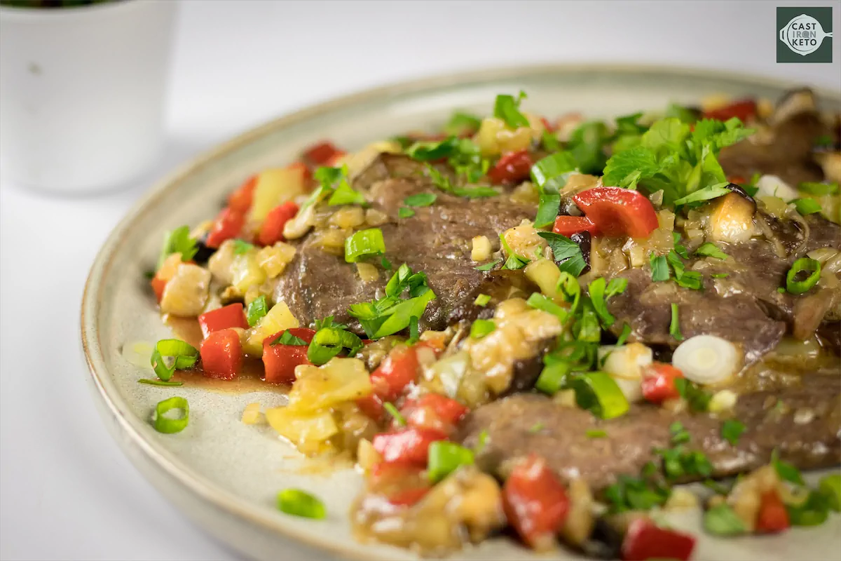 Beef steak topped with peppers and green onions, served on kitchen table.