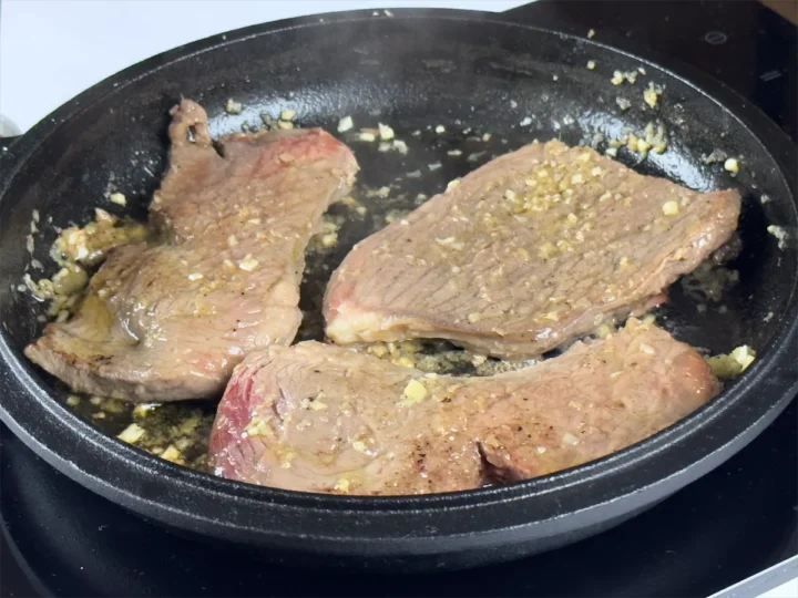 Steaks being cooked with ginger in a cast iron dish.