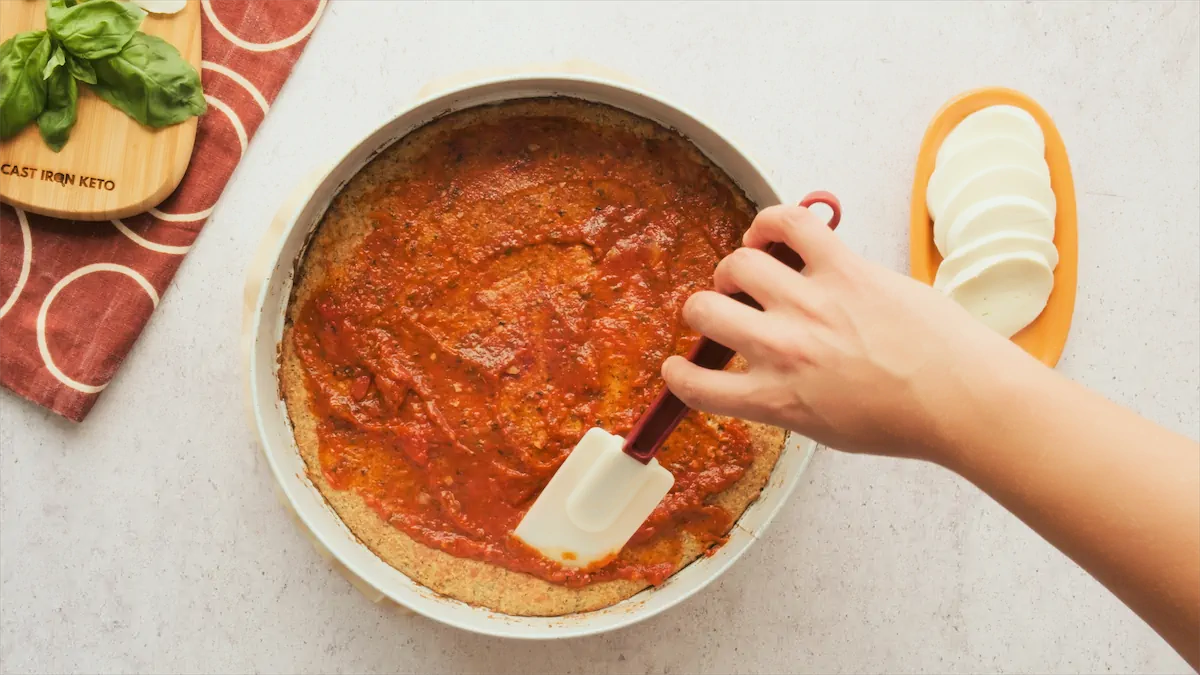 Spreading pizza sauce all over the crust.