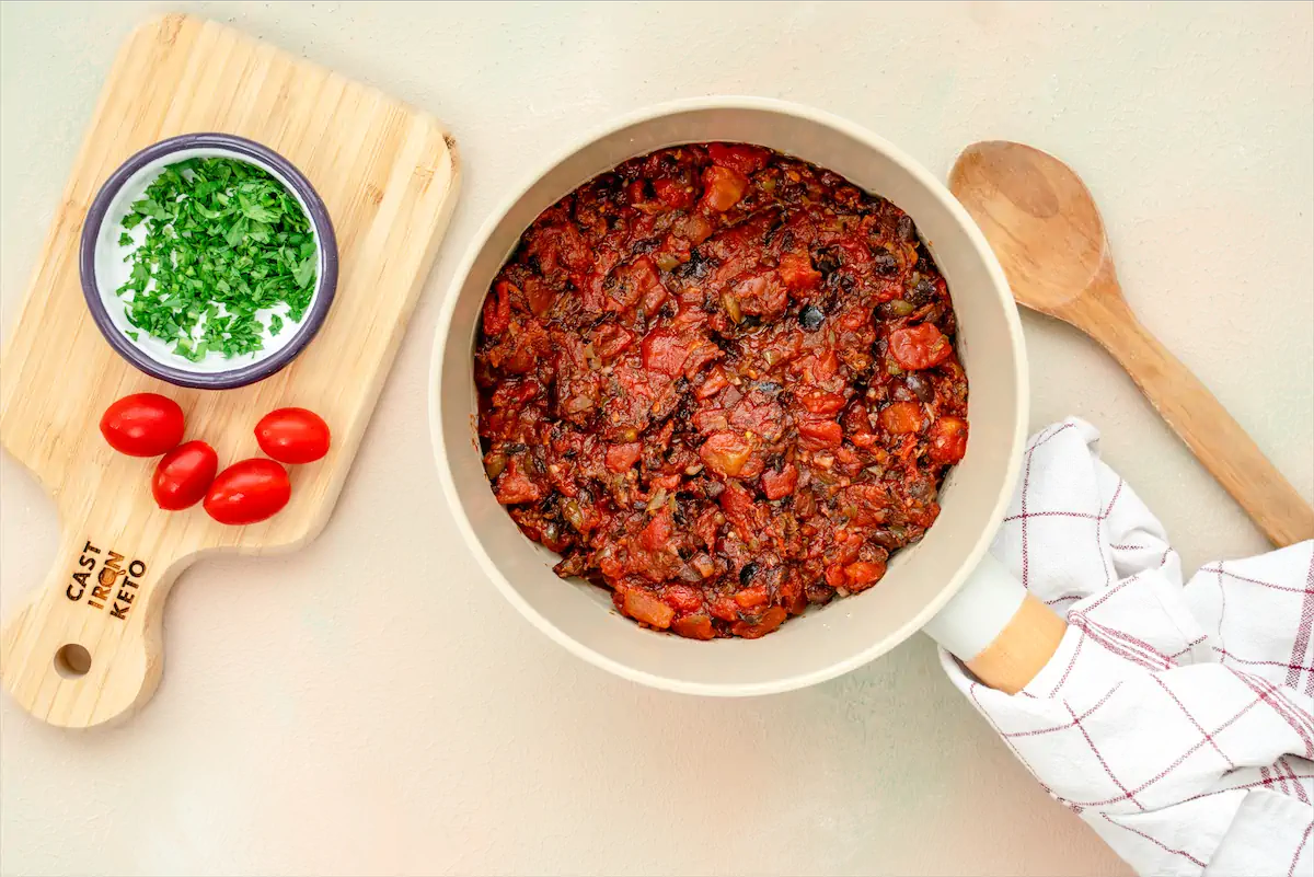 Keto tomato sauce containing anchovy on a pan accompanied by tomatoes and chopped coriander.