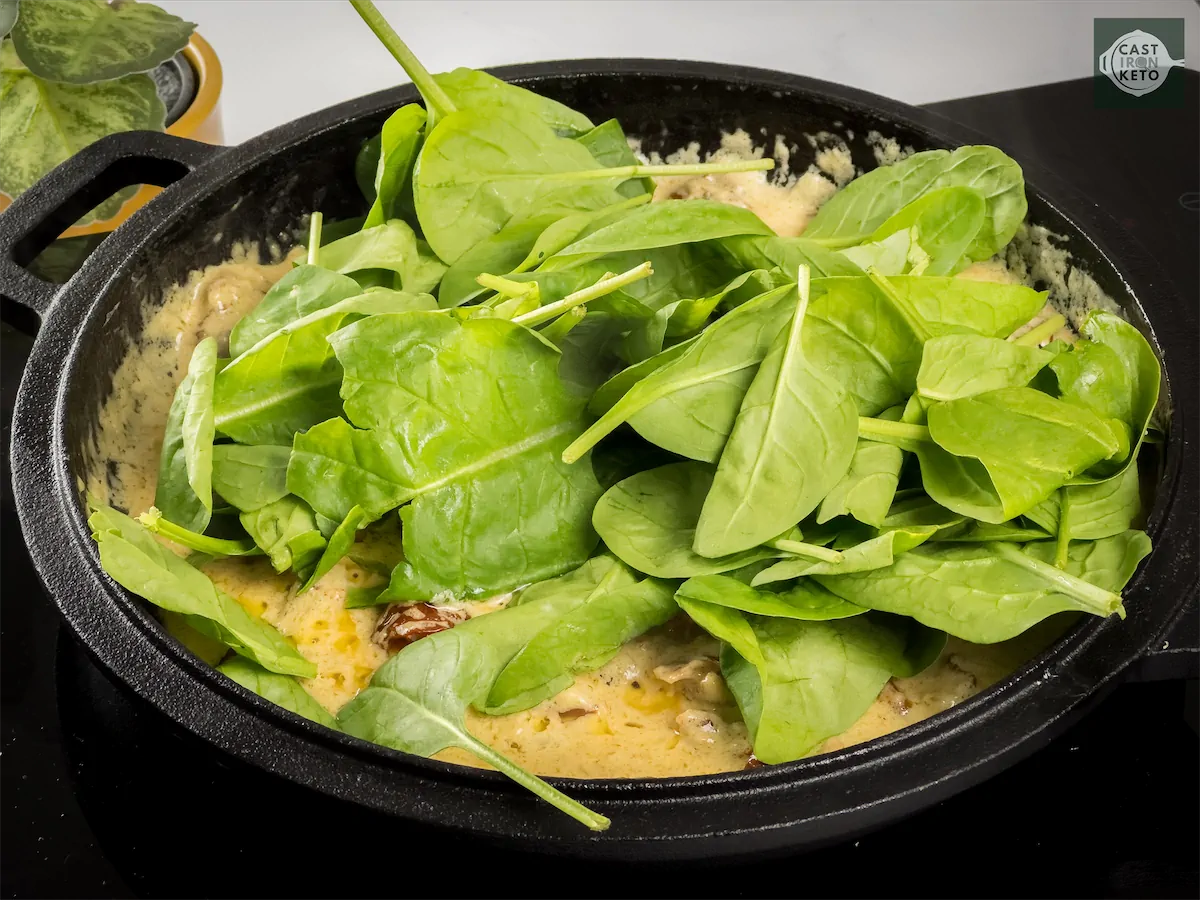 Spinach leaves added to the creamy dish made in a cast iron pan.