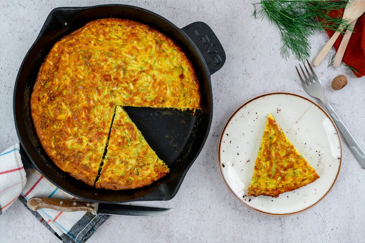 A slice of baked keto zucchini frittata served on a plate from a cast iron pan.