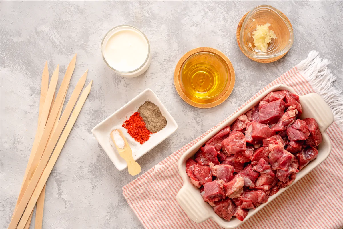 Ingredients like lamb cubes, heavy cream, olive oil, minced garlic, salt black pepper made ready on the table to make lamb shish kebab recipe.