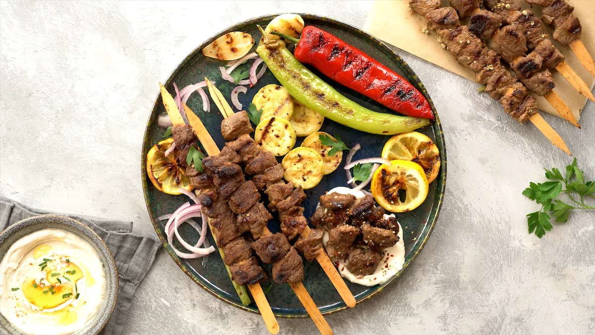 Freshly prepared Turkish lamb kebab in skewers served on a plate with other veggies.