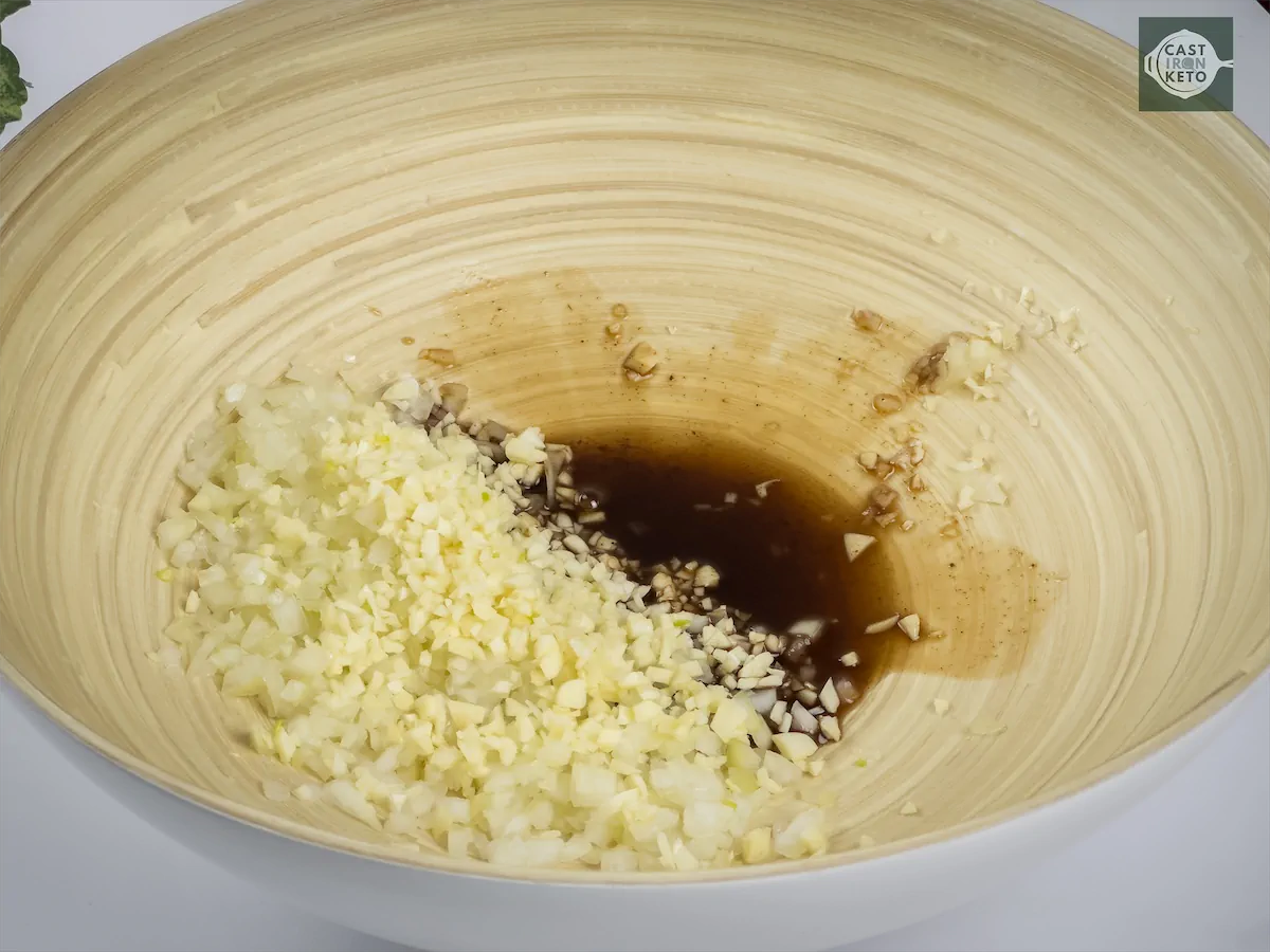 Chopped onion and garlic, soy sauce, and olive oil mixed in a bowl.