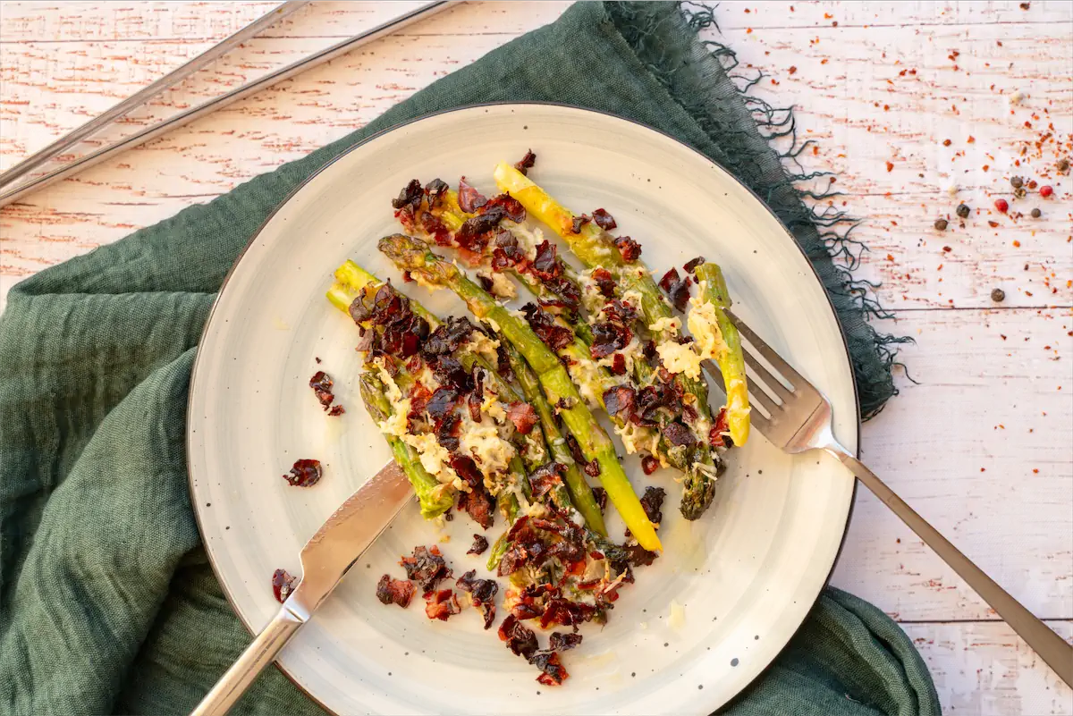 Baked asparagus and parmesan recipe served on a plate with cutleries.