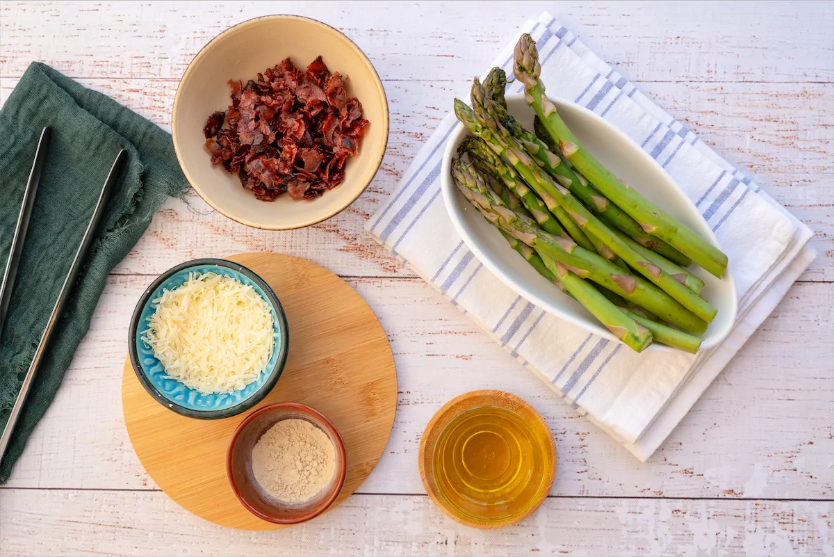 Ingredients like asparagus, bacon crumbs, grated parmesan cheese, ginger powder, and olive oil made ready on the kitchen table.