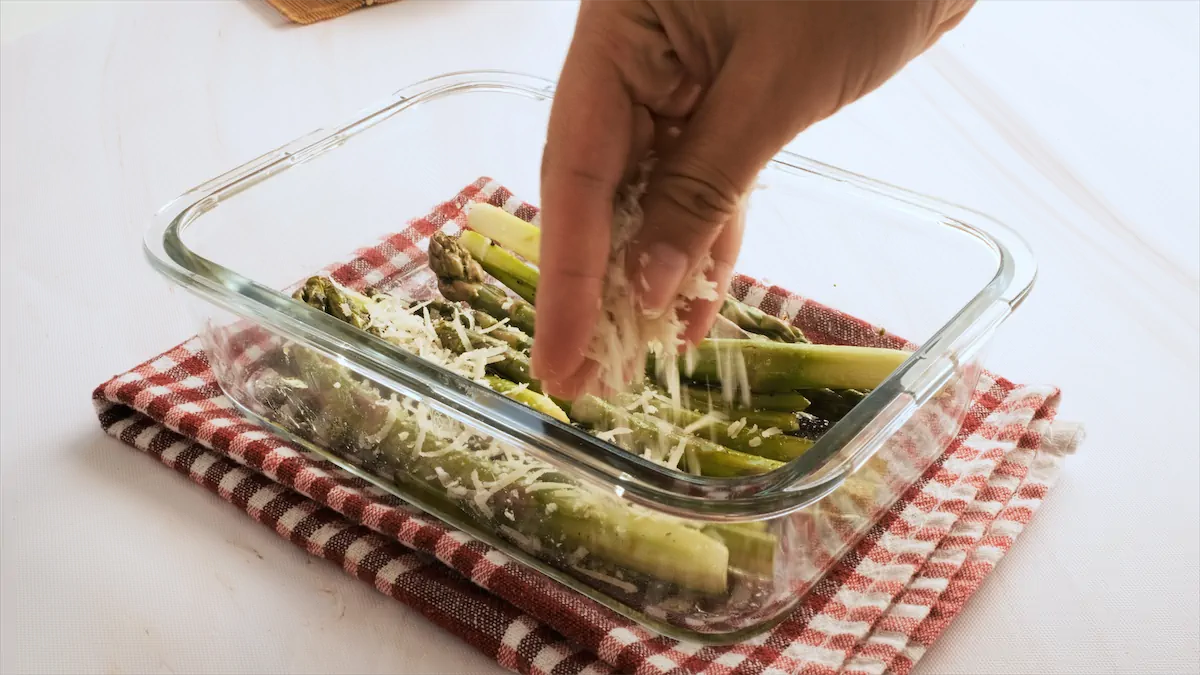 Adding parmesan cheese over asparagus on a baking dish.