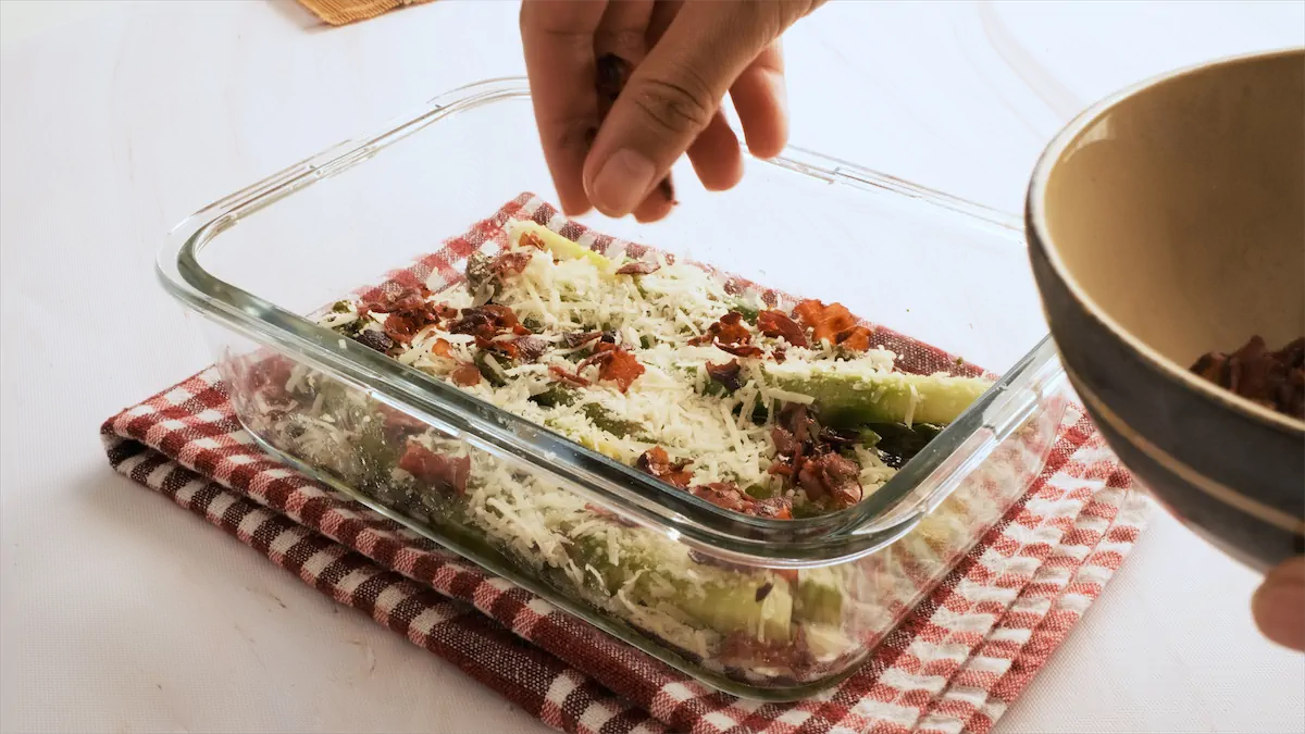 Adding crumbled bacon over asparagus and parmesan.