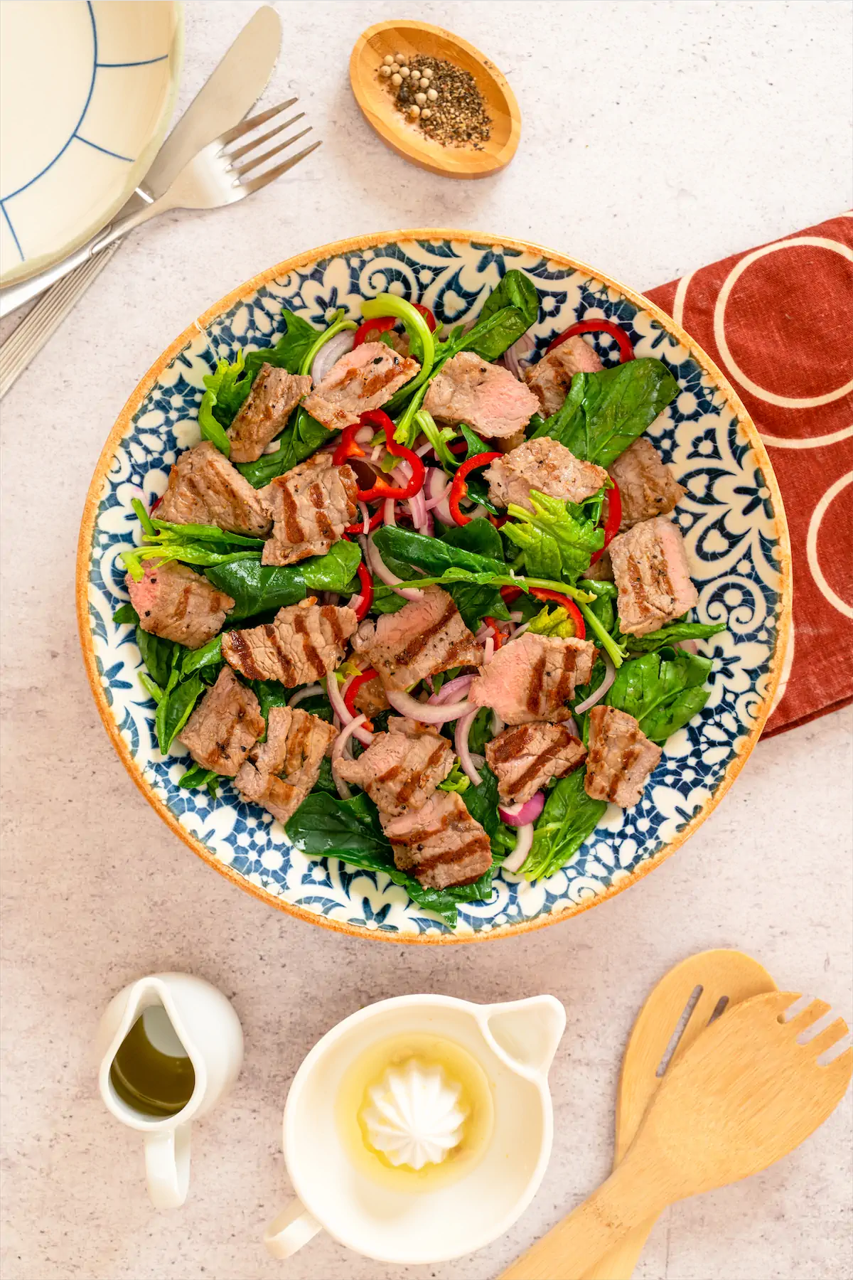 Salad containing steak, bell peppers, onions, spinach, olive oil.