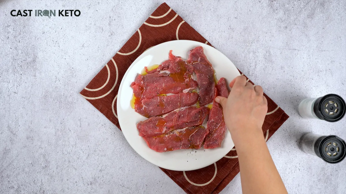 Seasoning steaks with salt, pepper, and olive oil.