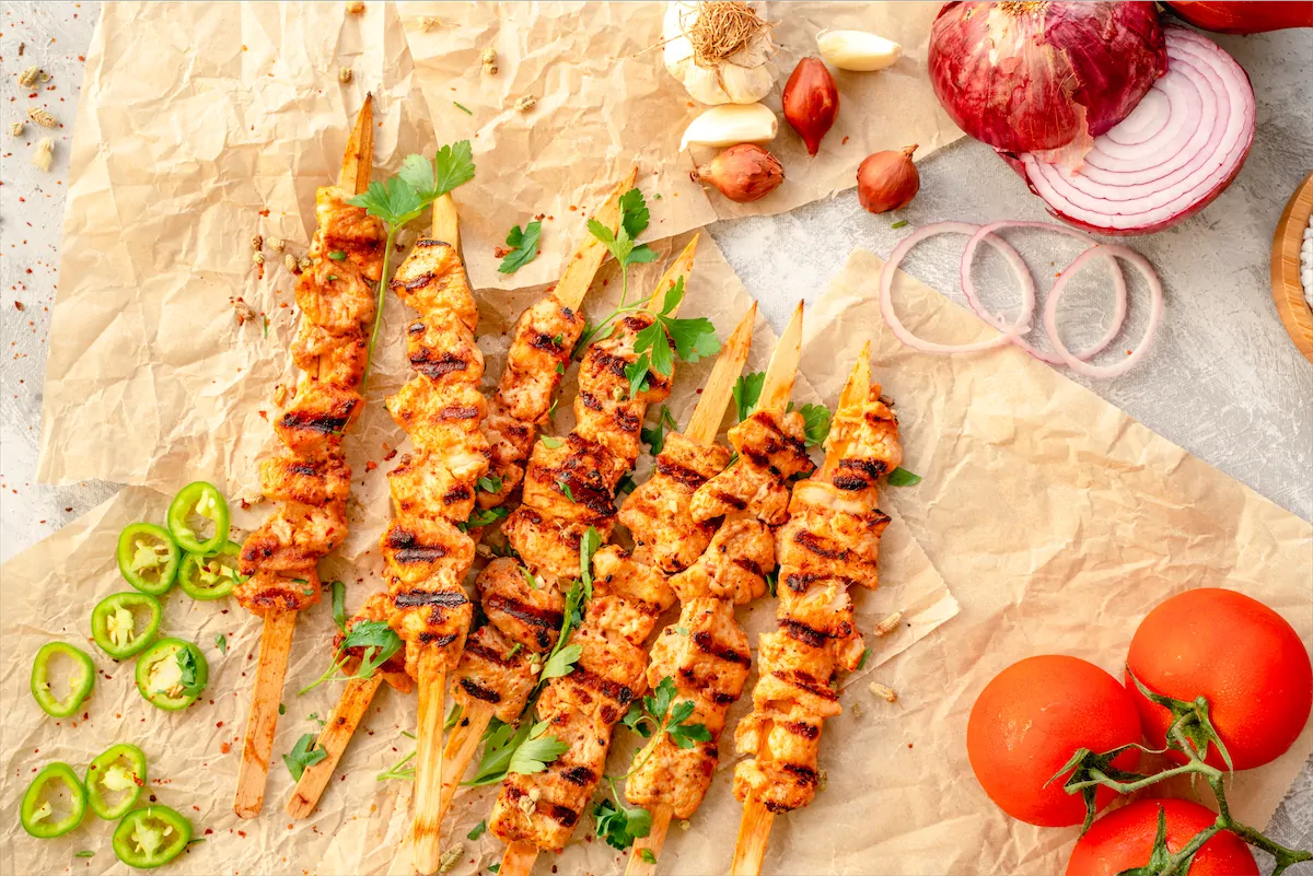 Skewers Chicken Kebab on kitchen table with tomatoes and onions.