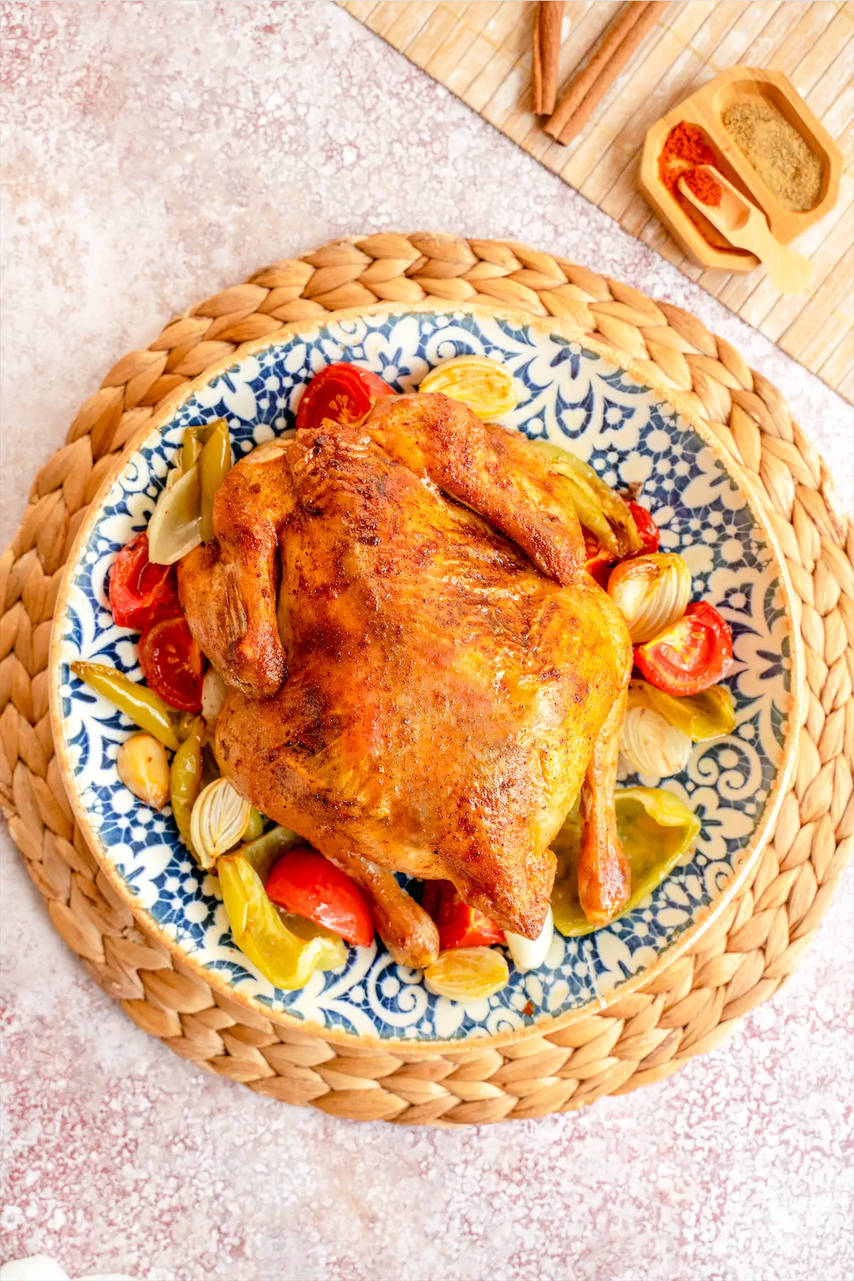 Roasted whole chicken with vegetables kept on a plate on kitchen table.