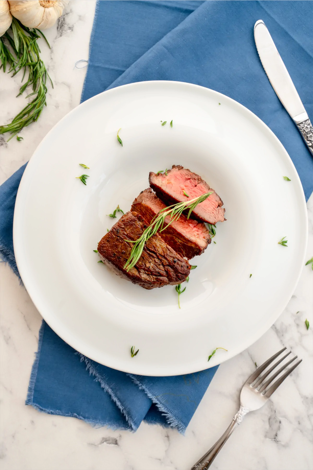 Slices of filet mignon on a plate, garnished with herbs.