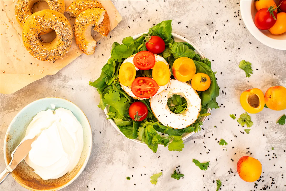 Halves of keto bagels served with greens and tomatoes.