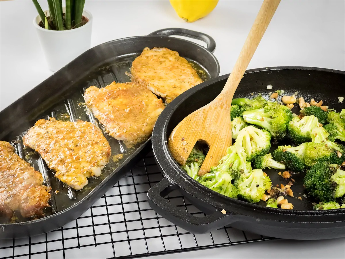 Baked pork chops in a cast iron grill pan and sautéed broccoli in a cast iron pan.