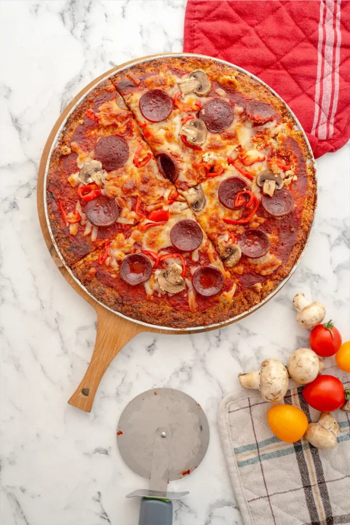 Keto pizza on a wooden pizza board.