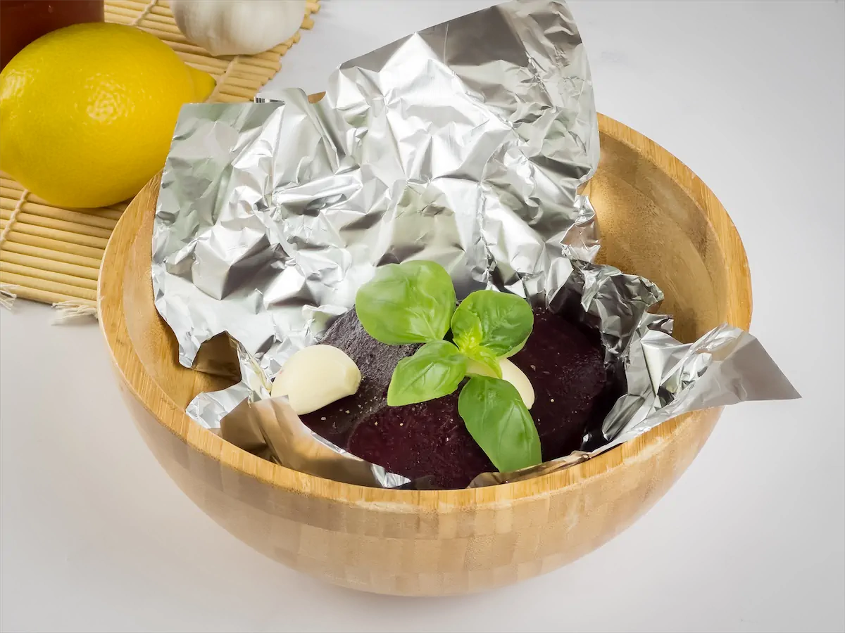 Beetroot slices, garlic cloves, oil, and basil leaves wrapped in an aluminum foil.