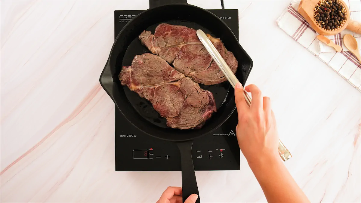 Flipping the steaks in a cast iron pan with the help of tongs.
