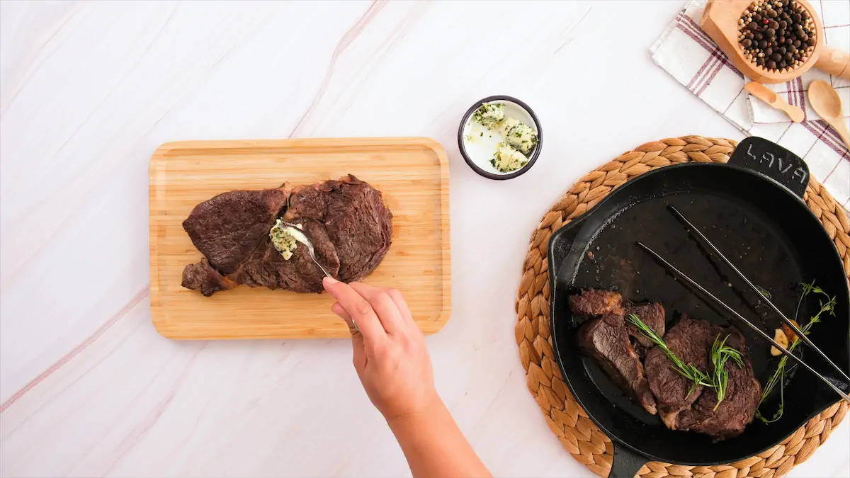 Adding herb butter using a spoonon top of a big steak.