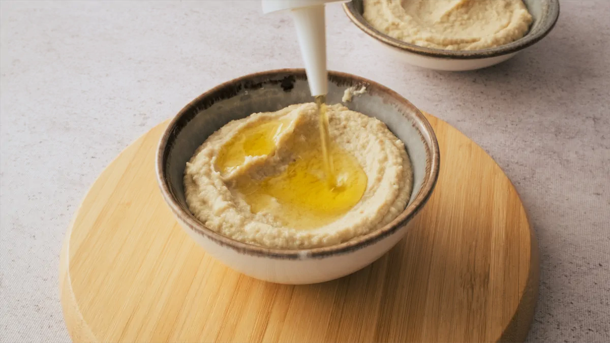 Drizzling olive oil over freshly prepared keto hummus in a bowl.