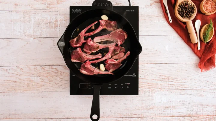 Lamb chops being cooked in a cast iron pan.