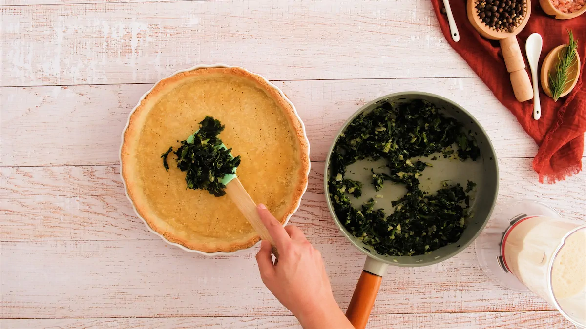 Adding spinach to the baked quiche crust.