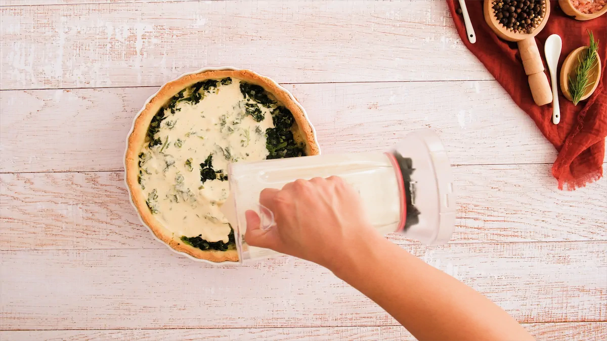 Adding the blended eggs and cream cheese to the spinach quiche.