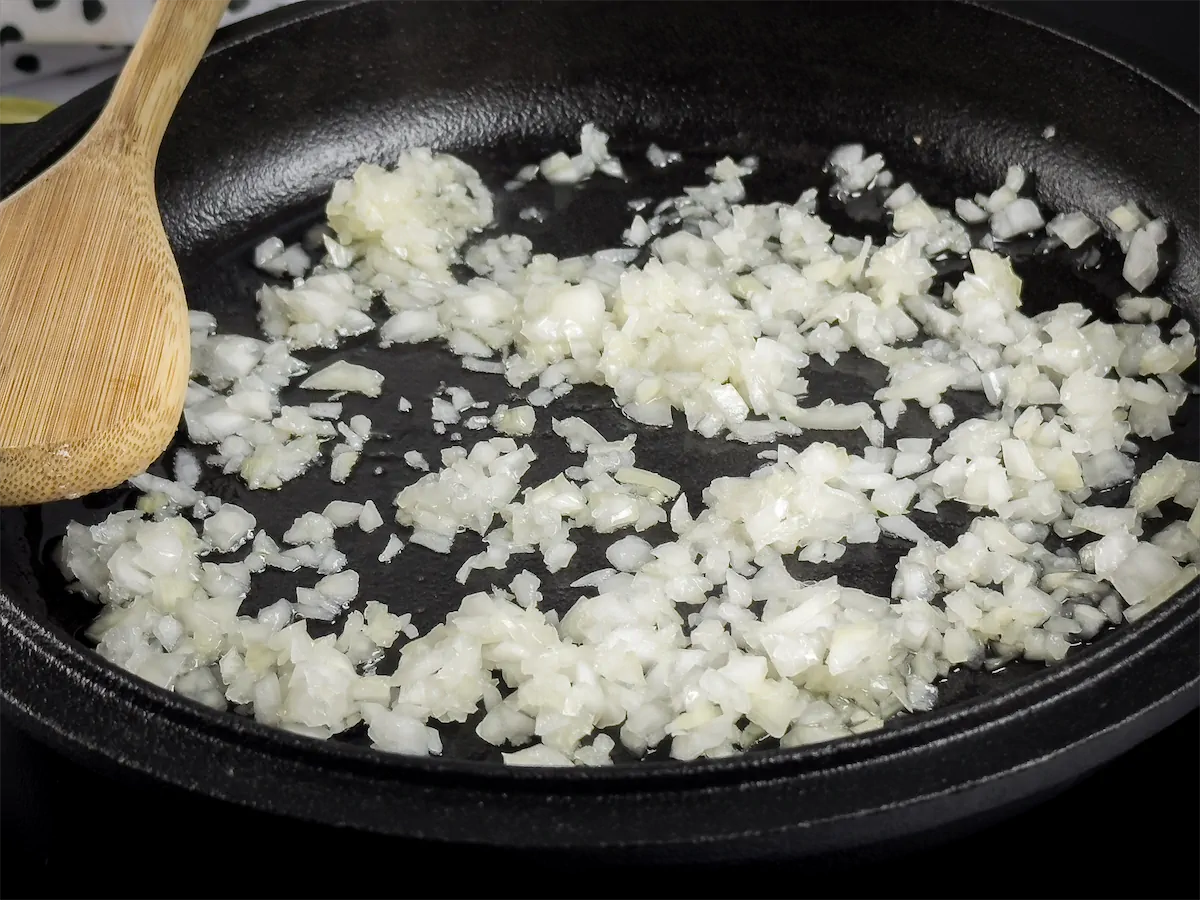 Chopped onions being cooked in a cast iron skillet.