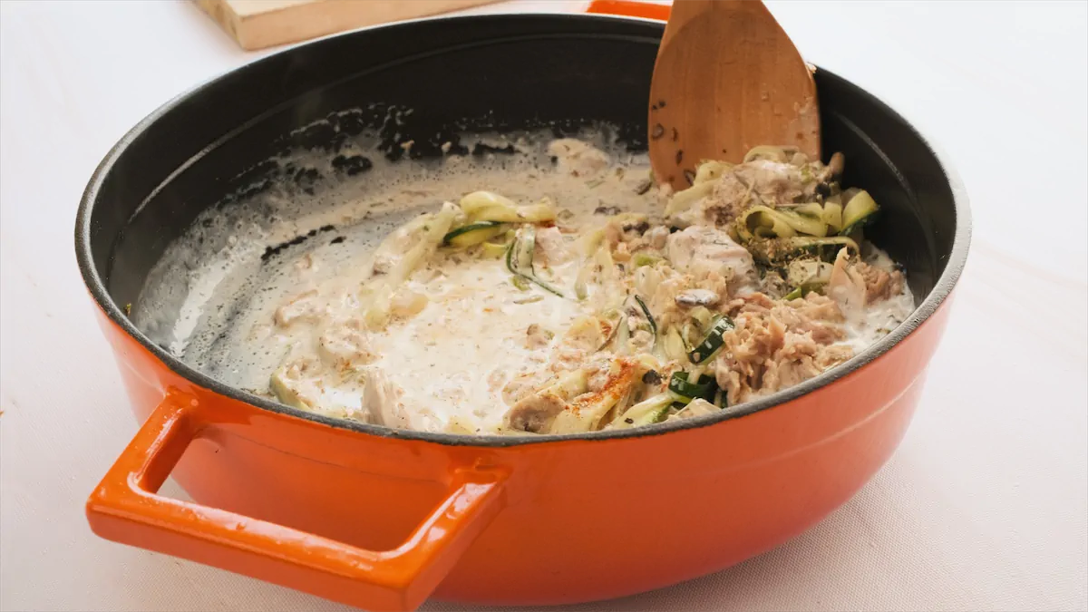Chicken broth and heavy cream added to a skillet containing tuna and vegetables.