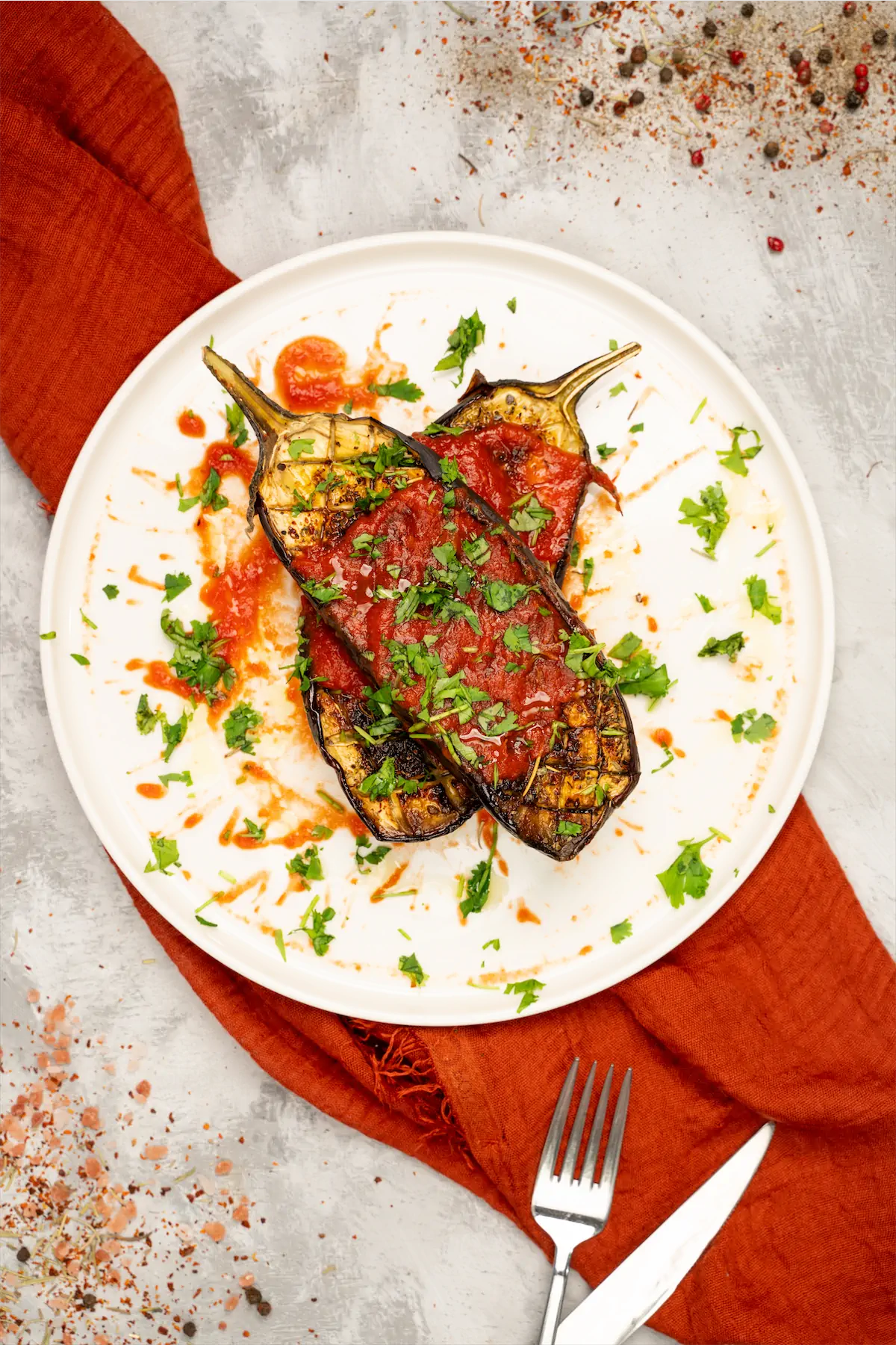 Homemade roasted eggplant recipe served on a plate topped with tomato sauce and chopped coriander leaves.