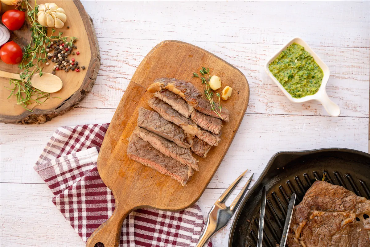 Slices of keto steaks on a wooden board on kitchen table next to dipping sauce.