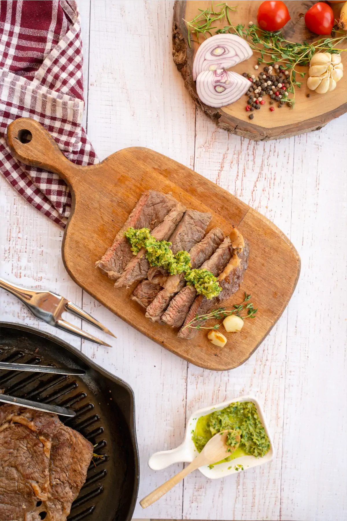 Steak slices on a table next to herbs and spices.