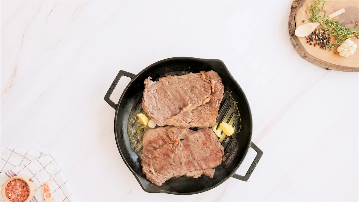Grilling steaks with butter in a cast iron grill.