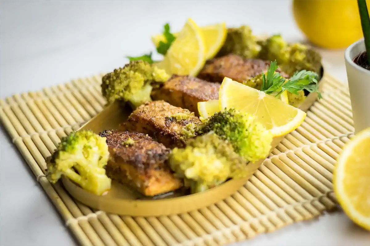 Blackened salmon in a tangy sauce, accompanied by broccoli and garnished with lemon slices.