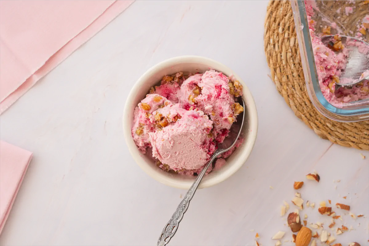 Ice cream made with cottage cheese, pecans and raspberries served in a bowl with a spoon.