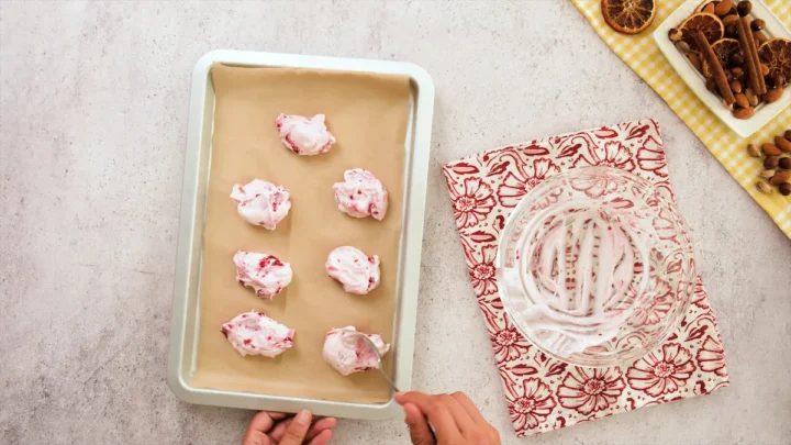 A mixture of yogurt and raspberries are portioned using a spoon on a tray for freezing.