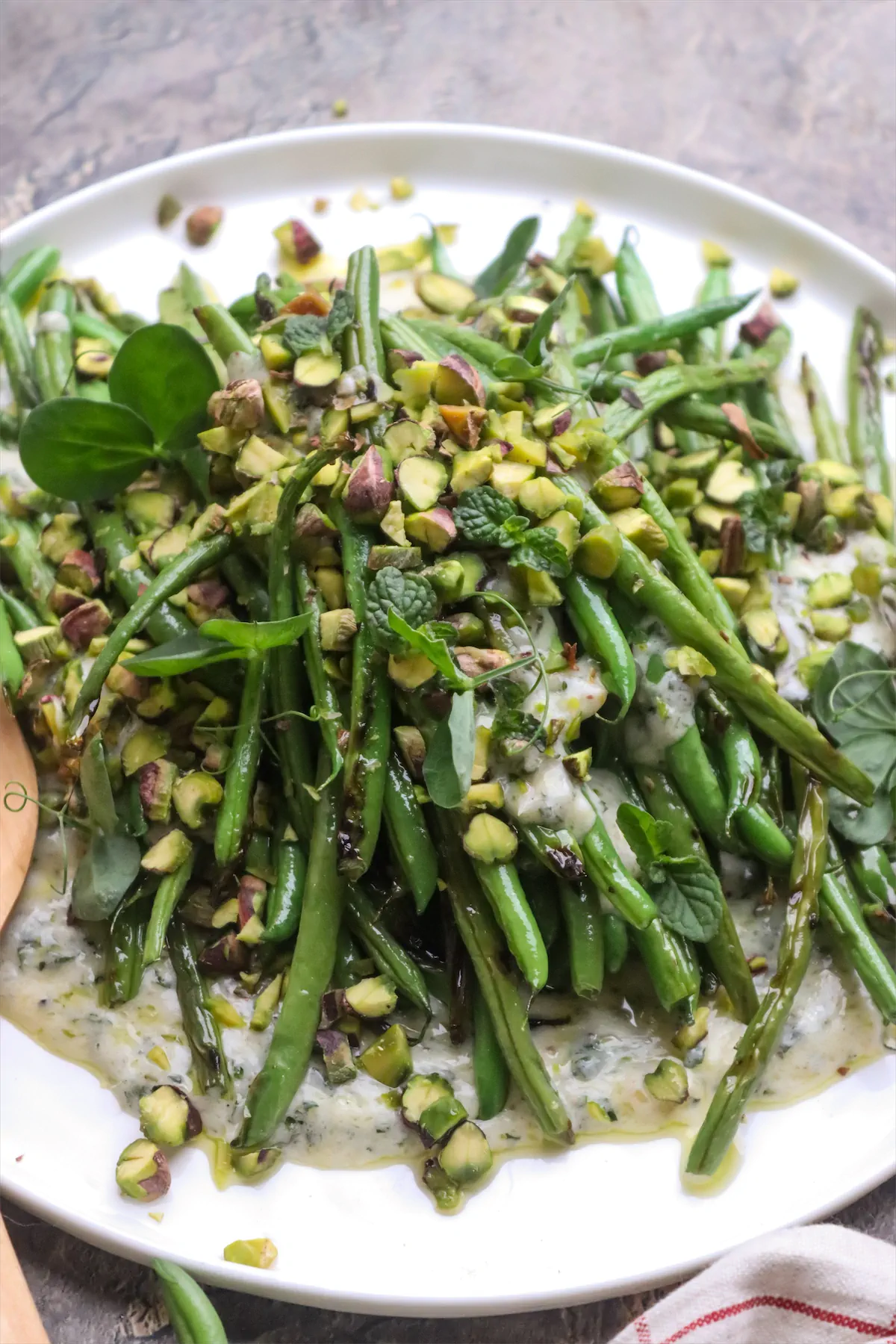 On the plate, a grilled green bean salad is dressed with yogurt and mint and garnished with pistachios