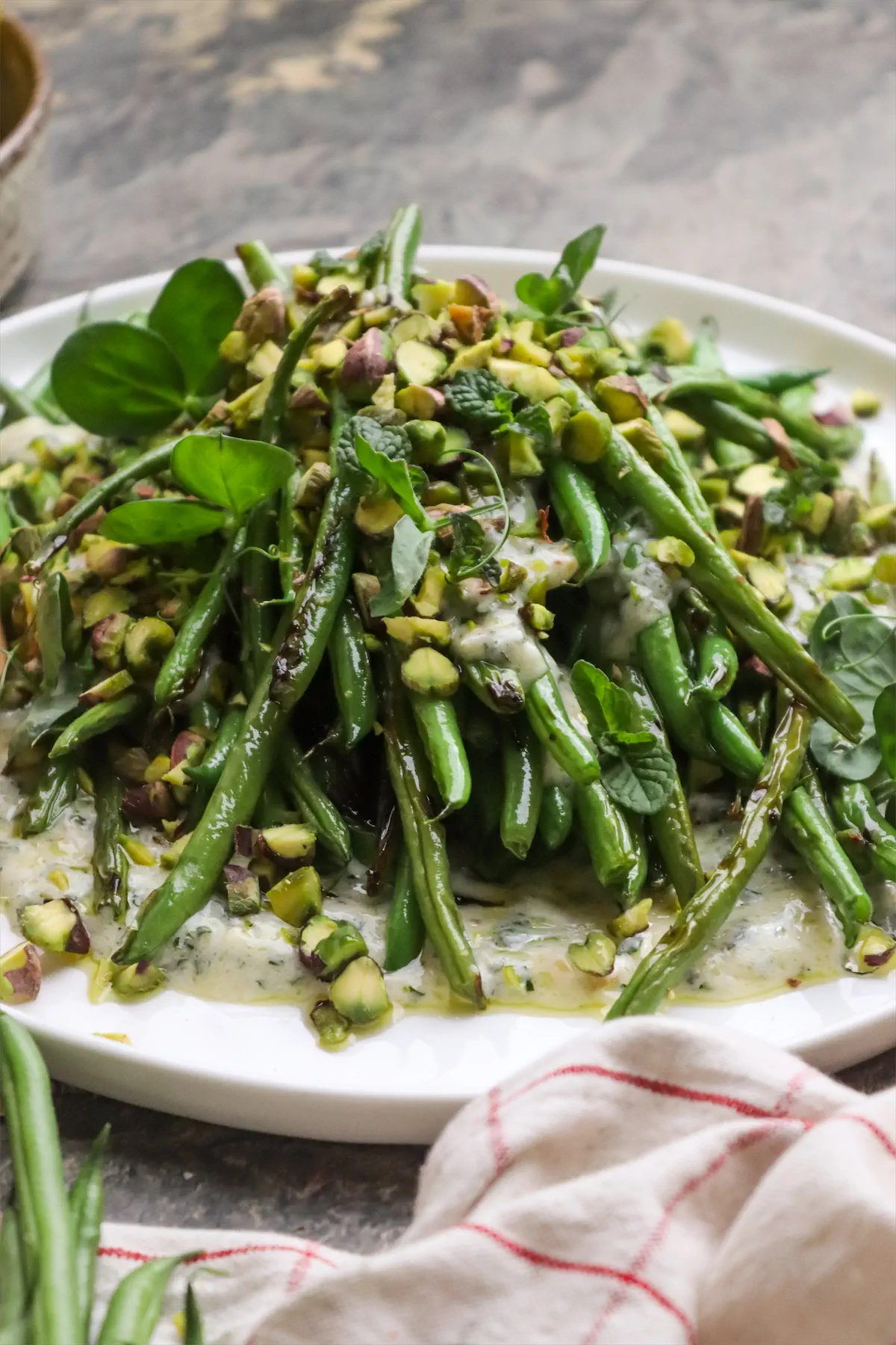 Low-carb grilled green bean salad with yogurt and mint-dressing topped with pistachios on a plate.