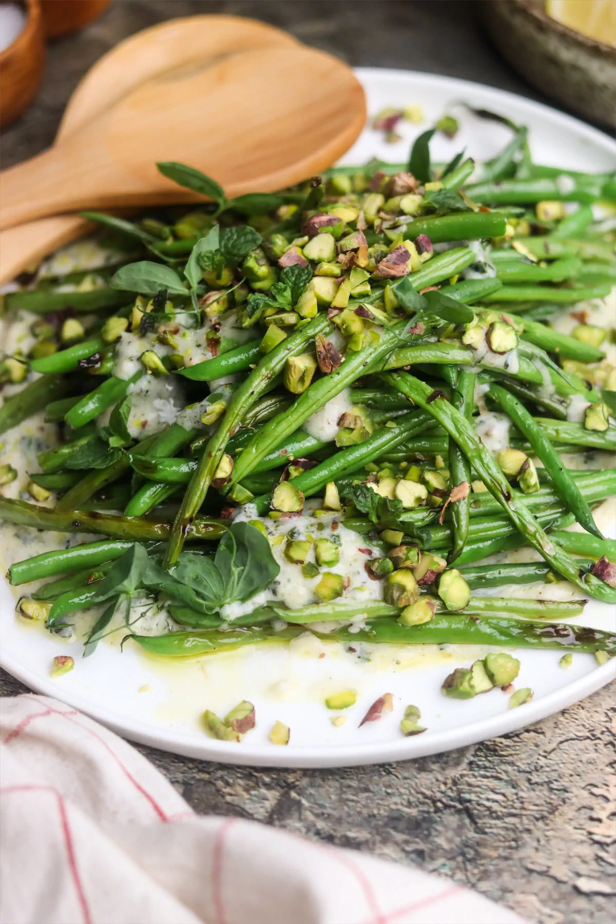 Grilled green beans on yogurt and mint dressing topped with nuts on a plate.