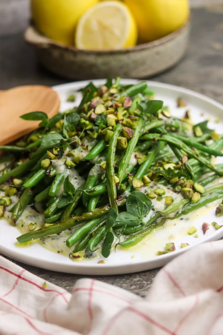 Homemade grilled green bean salad, with yogurt and mint dressing and garnished with pistachios on a plate.