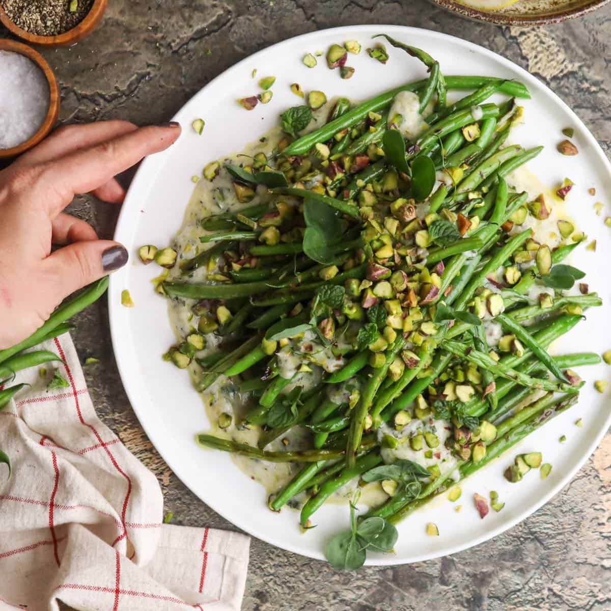 Grilled green bean salad on a bed of yogurt and mint dressing, garnished with pistachios, presented on a plate.